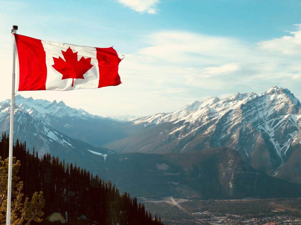 Canadian flag flying over mountain landscape, representing hope and new beginnings in this pre-arrival guide for newcomers to Canada.